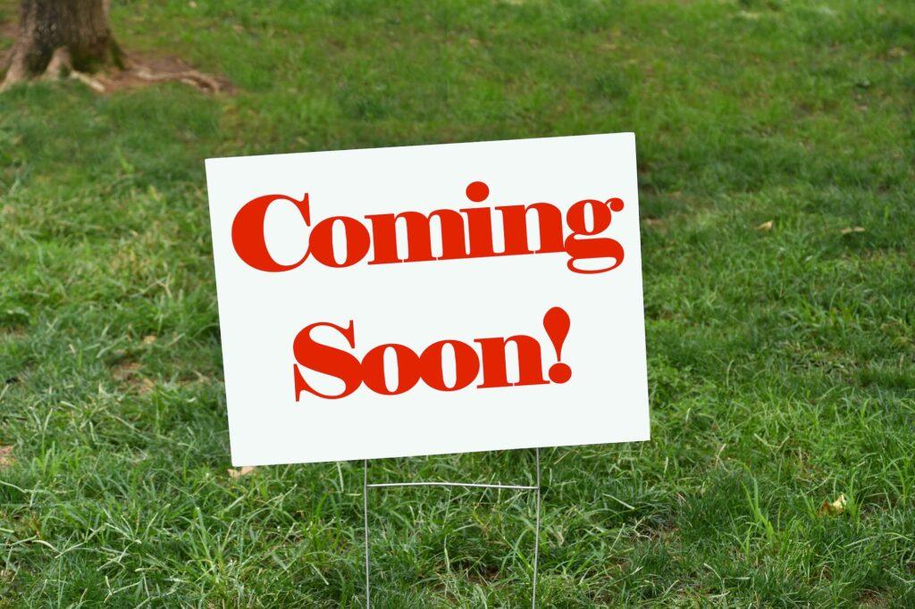 Coming Soon! sign in the grass announcing there will be a new addition in the near future.